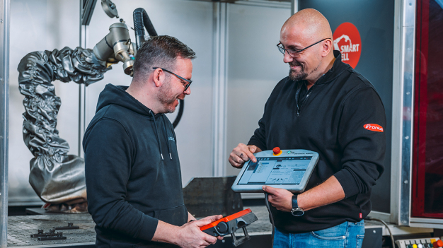 Fertigungsleiter Tony Meyer lässt sich von Fronius-Anwendungstechniker Andreas Plumeier zeigen, wie einfach das Teachen der Fronius SmartCell mit der Software SmartArc und dem SAEP-Handgriff funktioniert. (Bildnachweis: Christoph Große/pivopix im Auftrag von Fronius Deutschland GmbH)