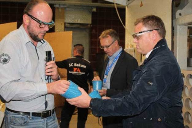 Ein blauer Topf bringt den Kreislauf in Schwung: Produktionsleiter Ulrich Lampe (links) erläuterte dem Lohner Bürgermeister Tobias Gerdesmeyer (rechts) im Rahmen der XXL-Werksführung, die Herstellung des neuen Reycling-Produktes. (Bild: Pöppelmann GmbH & Co. KG Kunststoffwerk-Werkzeugbau)