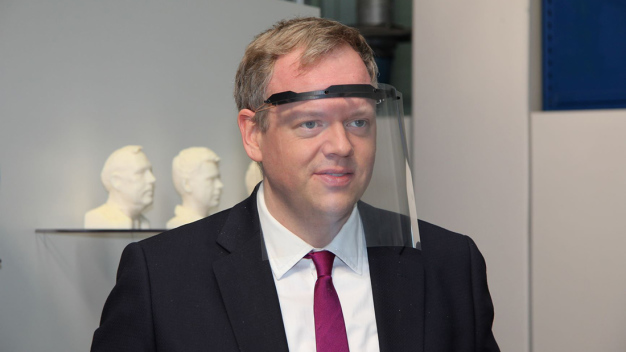 Landrat Dr. Matthias Neth probiert gleich einen Gesichtsschild aus, der aus einem gedruckten Träger, einer Tageslichtprojektorfolie und Gummiband besteht. (Foto: Ziehl-Abegg / Rainer Grill) 