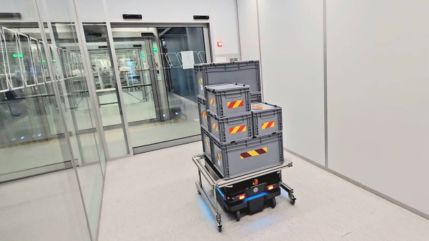 Autonome mobile Roboter, die per Funk die Schiebetüren öffnen, fahren automatisch in die Materialschleuse ein. / Autonomous mobile robots, which open the sliding doors by radio, enter the Material lock automatically.