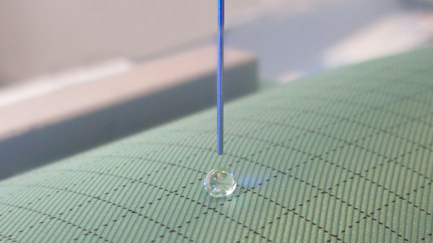 Auf den beschichteten Reinraumtextilien bilden sich runde Tropfen mit entsprechend großen Kontaktwinkeln aus. / Round drops with correspondingly large contact angles form on the coated cleanroom textiles. Auf den beschichteten Reinraumtextilien bilden sich runde Tropfen mit entsprechend großen Kontaktwinkeln aus. / Round drops with correspondingly large contact angles form on the coated cleanroom textiles.