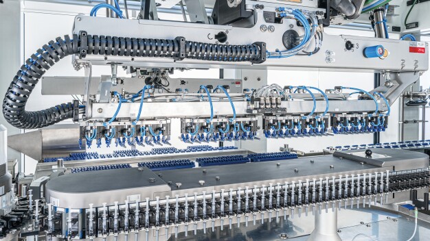 Über ein Zuführsystem gelangen die Spritzen vertikal ausgerichtet in die Verpackungslinie (untere Bildhälfte). Roboter platzieren die Produkte anschließend horizontal auf Transportmodule. (Foto: Gerhard Schubert GmbH)
