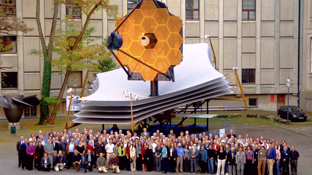 Gruppenbild unter dem Teleskop: Dieses Foto entstand aus Anlass eines James-Webb-Konsortium-Treffens und zeigt die Dimensionen des Weltraumobservatoriums. Das Modell dieses James Webb Space Telescope entspricht der Größe des Originals. Örs Hunor Detre / MPIA / This photo, taken on the occasion of a James Webb Consortium meeting, shows the dimensions of the James Webb Space Telescope. The model of this telescope corresponds to its original size. © Örs Hunor Detre / MPIA 